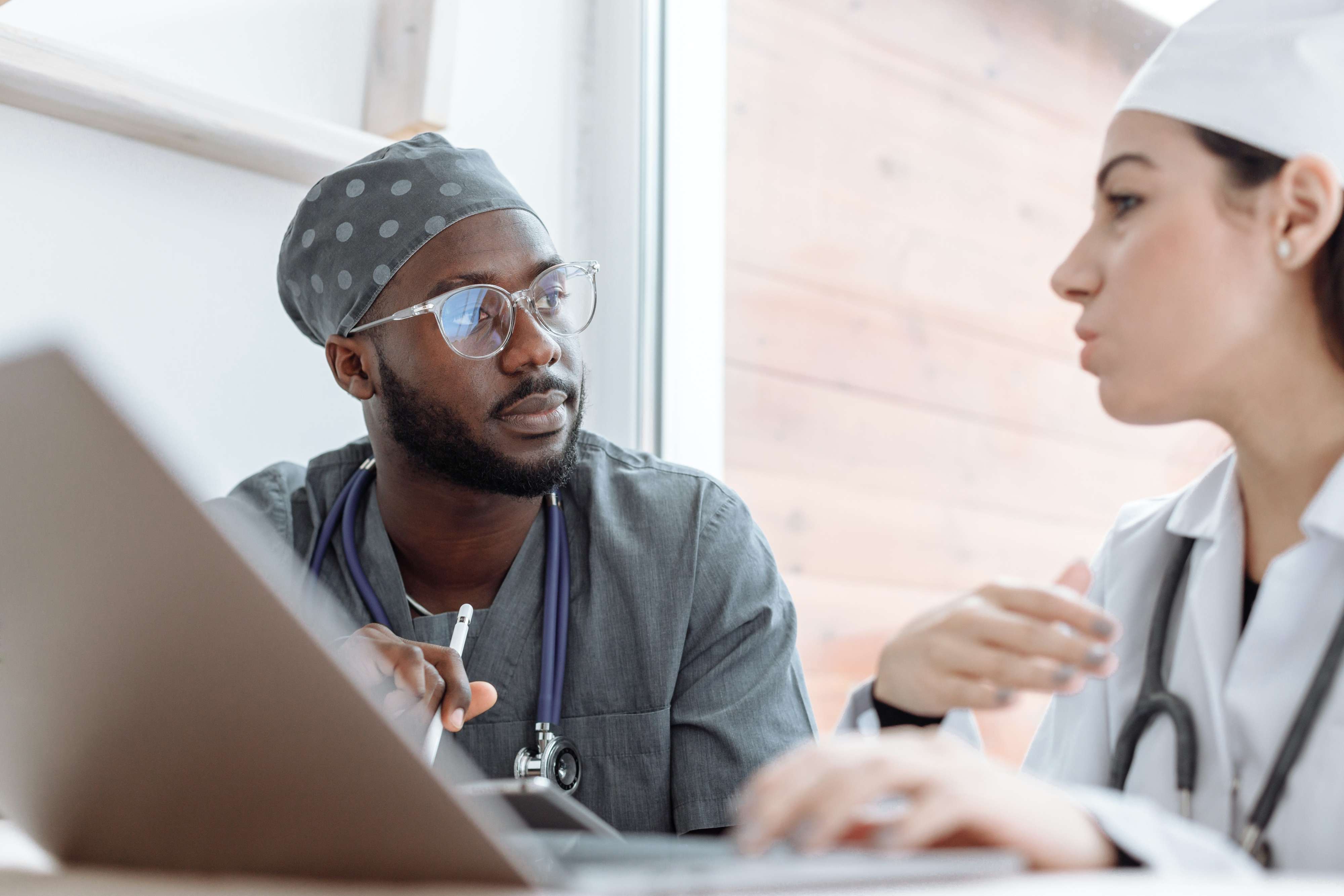 Two medical professionals discuss while seated at a laptop.