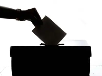 Person casting a vote into a ballot box silhouette.