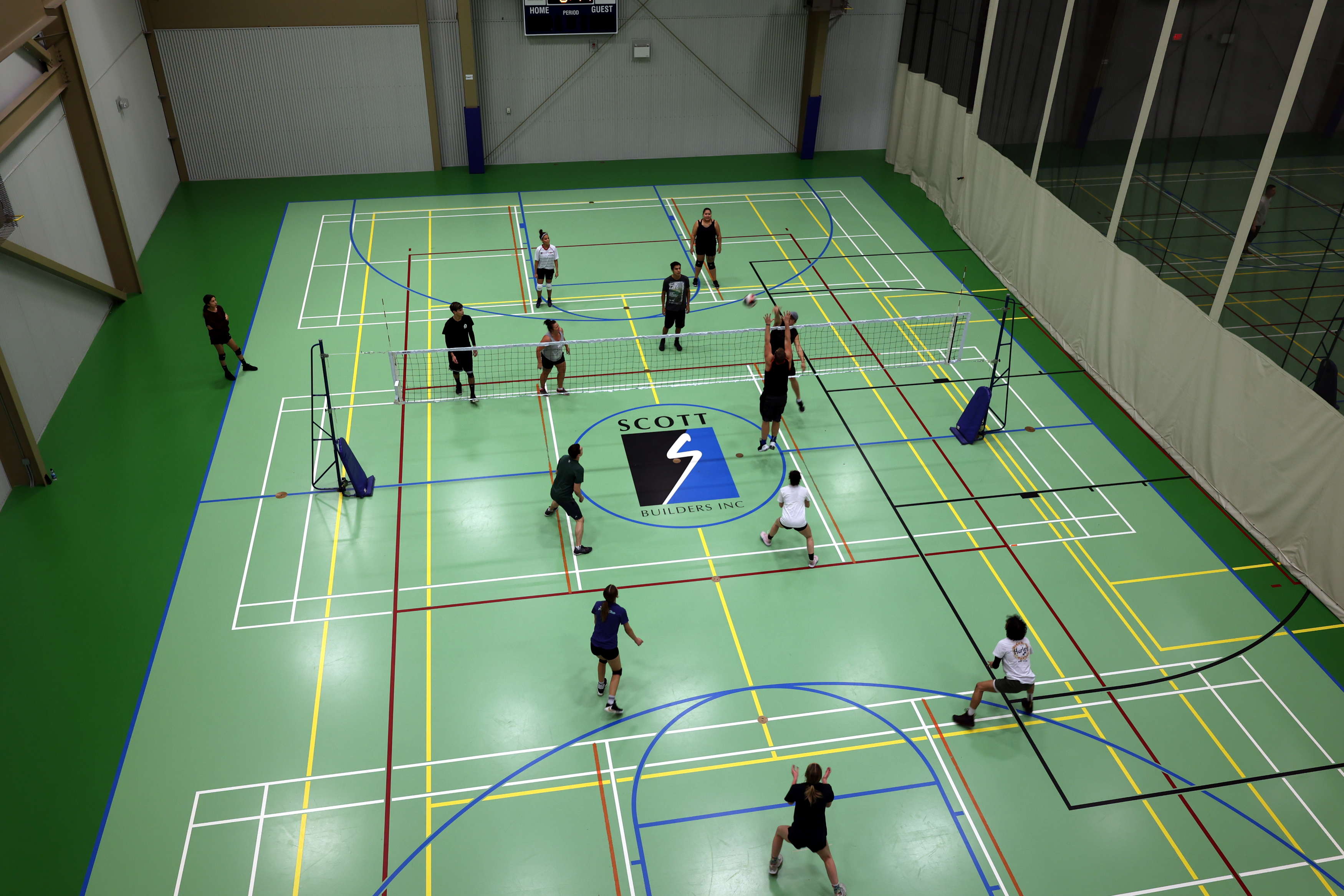 Players engaging in a volleyball game indoors on a green court with basketball lines.
