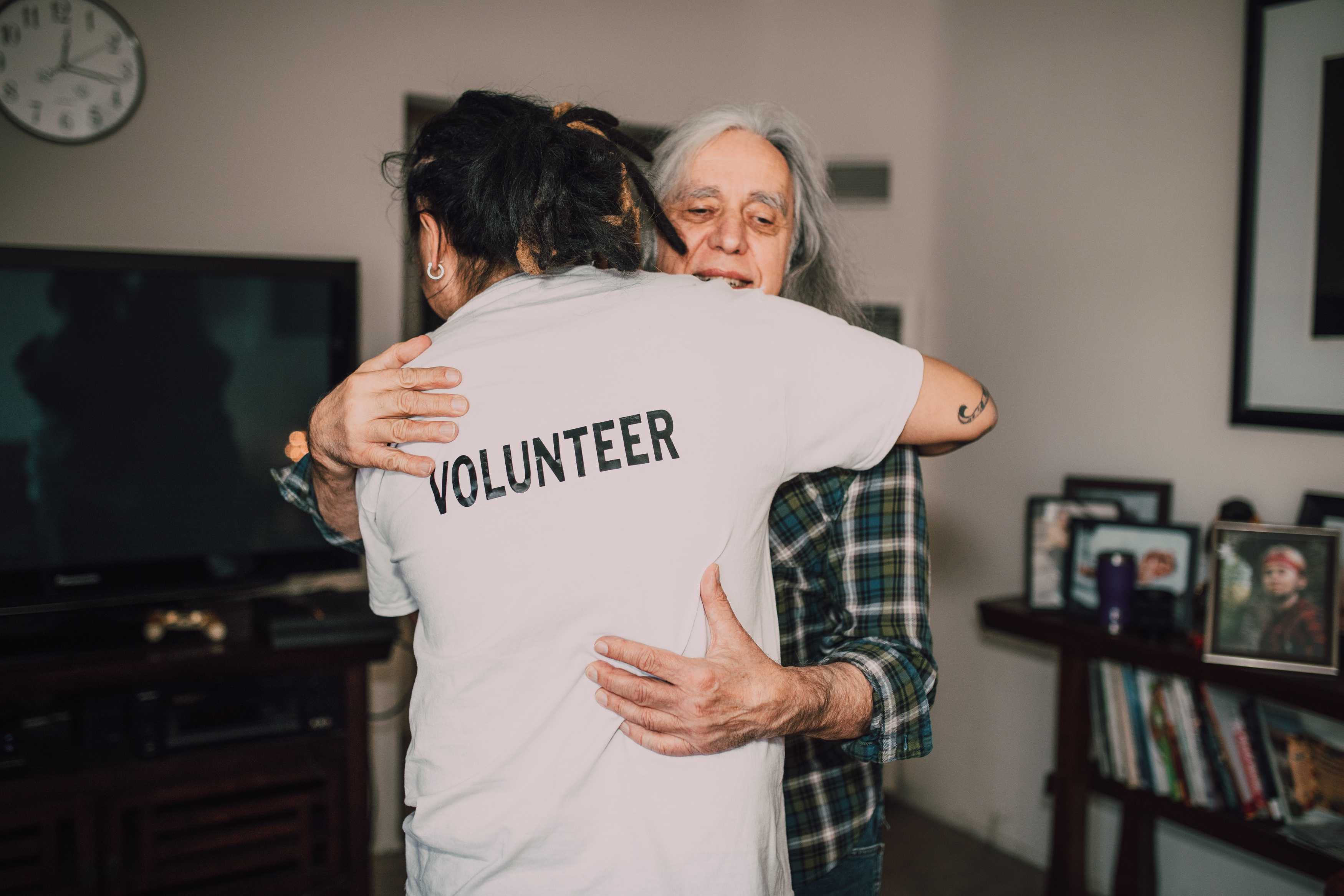 A volunteer hugs a senior in their home.