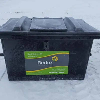 Black used cooking oil bin with "Redux" label; snow-covered ground.