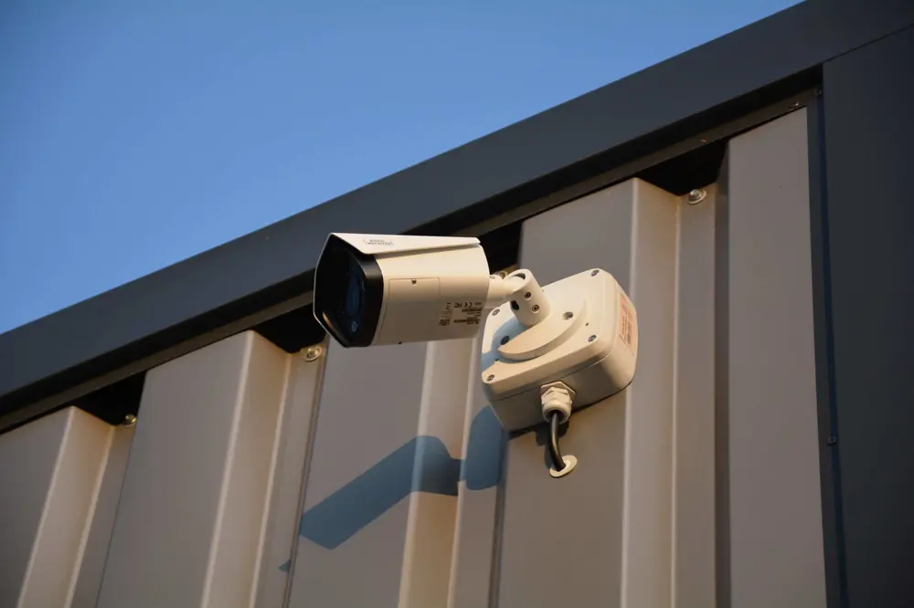 Surveillance camera mounted on a gray metal wall, angled for monitoring.